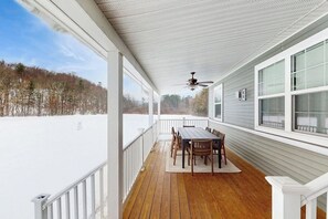 Eine überdachte Veranda mit Holztisch und -stühlen, großen Fenstern und Blick auf eine verschneite Landschaft.