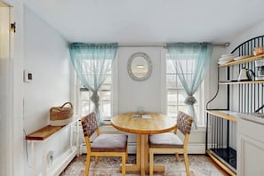 A small dining area with a round wooden table, two chairs, a wall-mounted mirror, and a shelf with dishes. - Cozy updated apartment: near skiing, hiking, shops & dining (Waterbury)