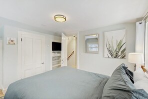 A bedroom with a bed, a bedside lamp, a door, a staircase, and a wall-mounted artwork. - Cozy updated apartment: near skiing, hiking, shops & dining (Waterbury)