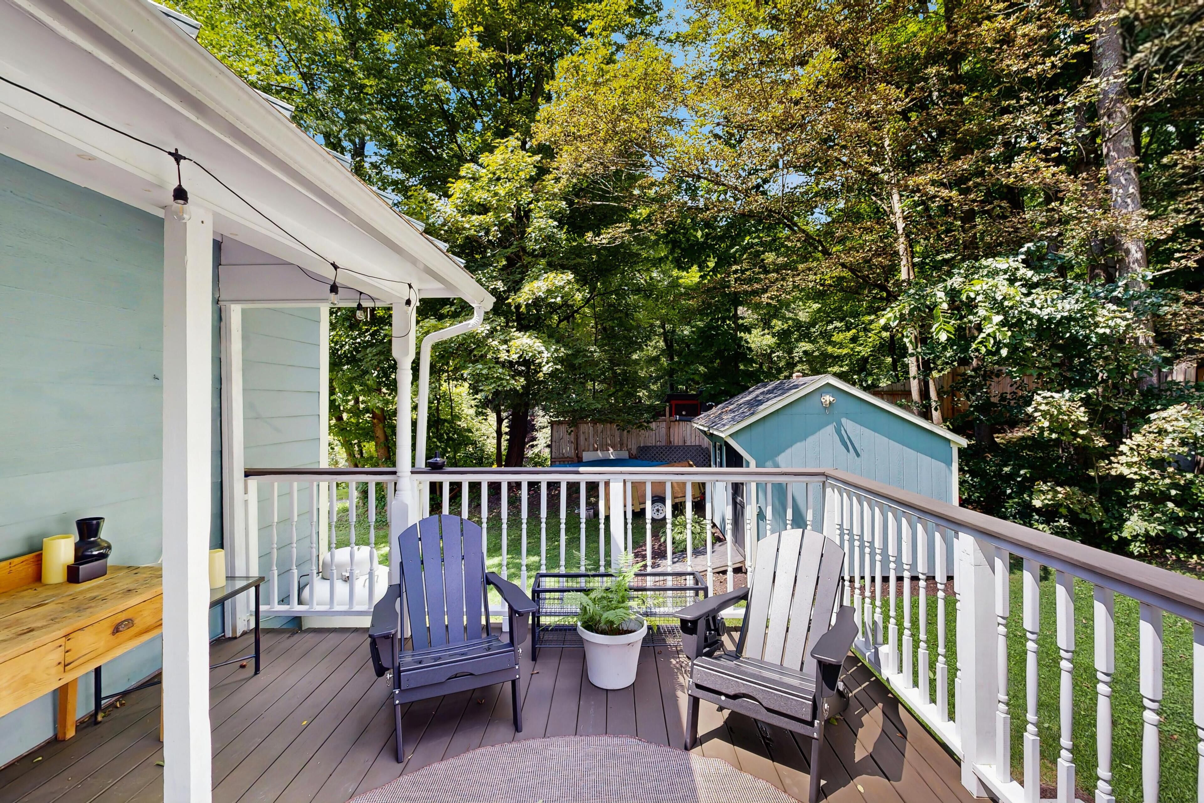 A wooden deck with outdoor furniture, a covered porch, and a small shed in a wooded area.