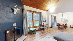A room with a wooden ceiling, a fireplace, a dining area with a table and chairs, and a window with curtains. - Ski-in/shuttle-out condo w/WiFi, fireplace, balcony, & newly renovated kitchen (Killington)