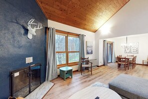 Ein Zimmer mit Holzbalkendecke, Kamin, Essbereich mit Tisch und Stühlen sowie einem Fenster mit Vorhängen.