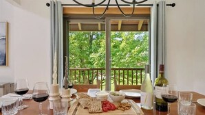 A dining table set for two with a view of trees through a glass door. - Ski-in/shuttle-out condo w/WiFi, fireplace, balcony, & newly renovated kitchen (Killington)