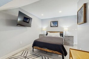 Ein Schlafzimmer mit einem Bett, Nachttischen, einem an der Wand montierten Fernseher und einem gerahmten Bild.