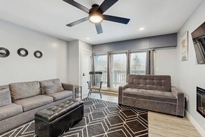 Ein modernes Wohnzimmer mit einer Couch, einem Sessel, einem Hocker und einem Deckenventilator.