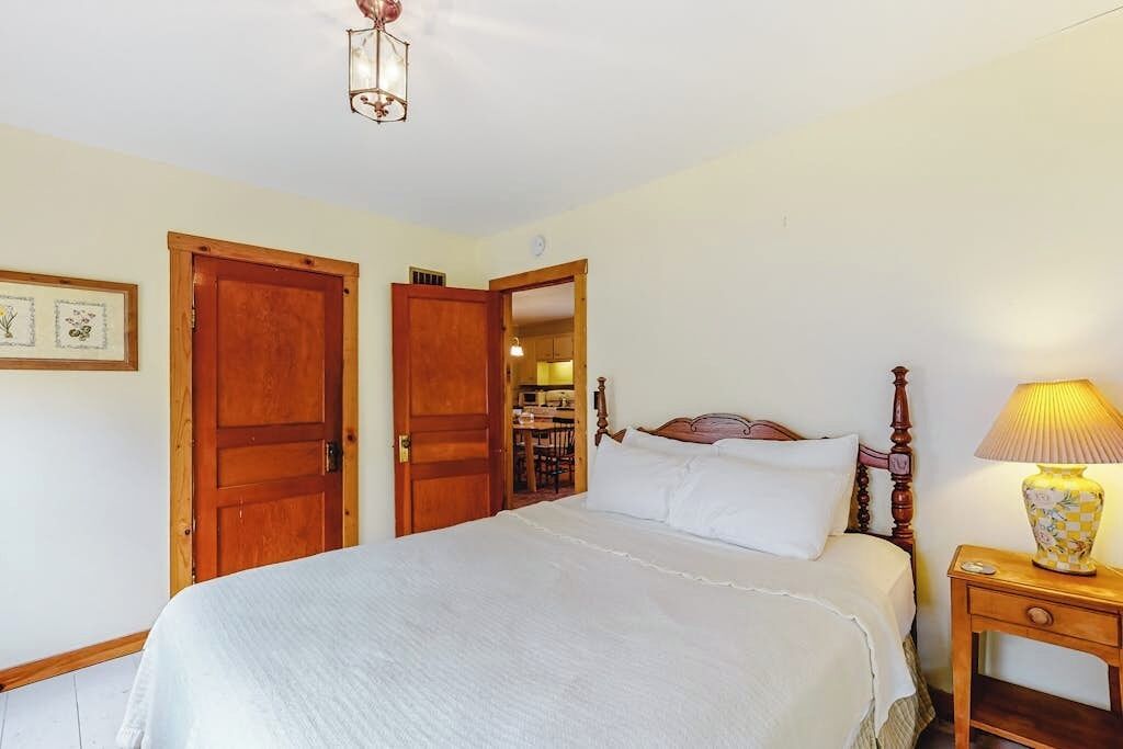 A bedroom with a bed, wooden doors, a nightstand, and a lamp.