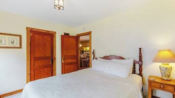 A bedroom with a bed, wooden doors, a nightstand, and a lamp.