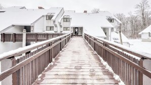 A snow-covered wooden bridge leading to a row of white buildings with sloped roofs. - Ski-in/out condo with  pool, hot tub, sauna & fast WiFi (Killington)