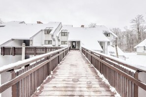A snow-covered wooden bridge leading to a row of white buildings with sloped roofs. - Ski-in/out condo with  pool, hot tub, sauna & fast WiFi (Killington)