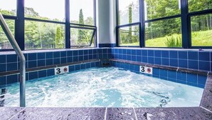 A hot tub with a view of a forest through large windows. - Ski-in/out condo with  pool, hot tub, sauna & fast WiFi (Killington)