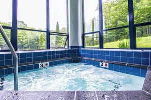 A hot tub with a view of a forest through large windows. - Ski-in/out condo with  pool, hot tub, sauna & fast WiFi (Killington)