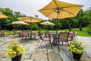 An outdoor patio with stone flooring, multiple tables with chairs, and large umbrellas. - Ski-in/out condo with  pool, hot tub, sauna & fast WiFi (Killington)