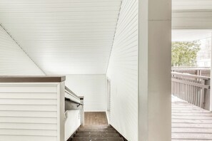 Una escalera estrecha con paredes blancas y una terraza de madera al exterior.