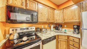 A kitchen with wooden cabinets, a microwave, a stove, a dishwasher, and a coffee maker. - Resort condo with mountain views, full kitchen, and free WiFi (Killington)