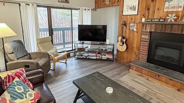 A living room with a TV, a fireplace, a guitar, and a bookshelf. - Resort condo with balcony & shared seasonal amenities - close to skiing (Killington)