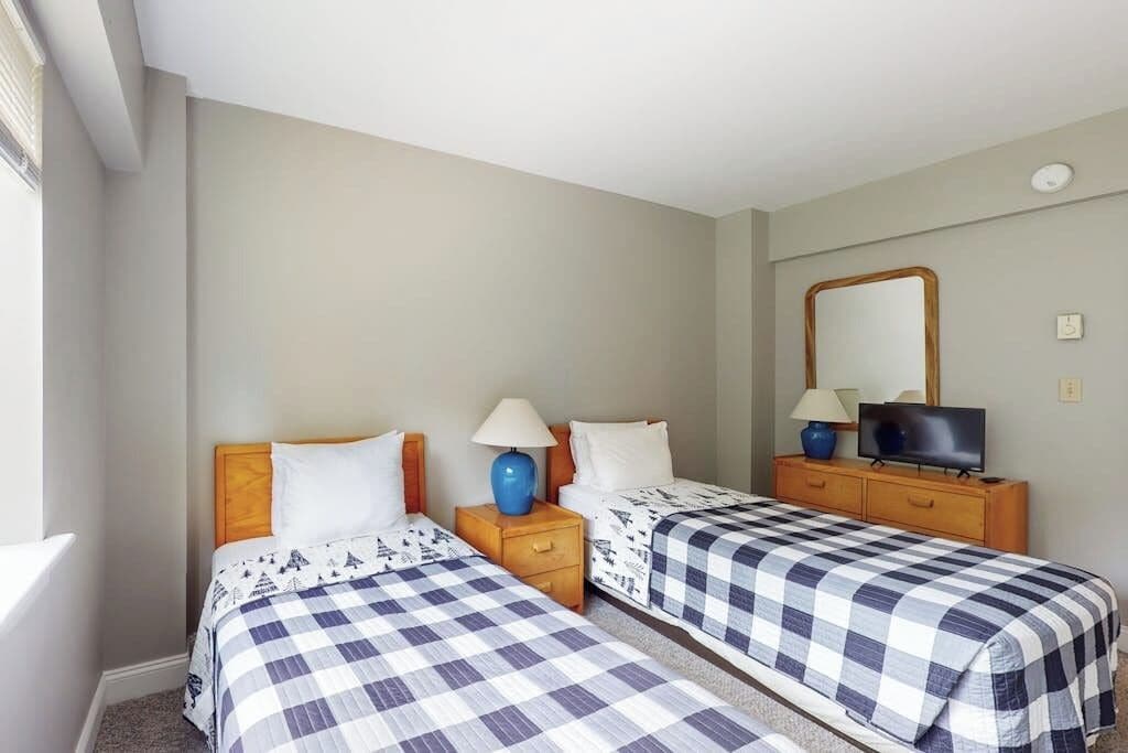 Habitación de hotel con dos camas, televisor, espejo y cómoda.