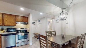 A modern kitchen with stainless steel appliances, wooden cabinets, and a dining area with a large table and chairs. - Resort condo with balcony & shared seasonal amenities - close to skiing (Killington)