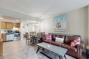 Eine moderne Küche mit Holzschnitzschränken, ein Essbereich mit Tisch und Stühlen, ein braunes Ledersofa mit Zierkissen und ein an der Wand befestigtes Schild.