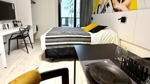 A hotel room with a bed, a desk, a chair, a TV, and a window with a view of buildings. - CloudBA Fitz Roy Apartments (Buenos Aires)