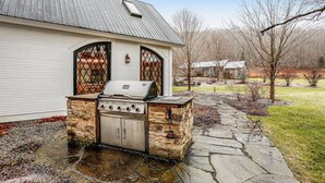 Una parrilla de piedra adosada a una casa, con un camino de piedra que la lleva hacia ella.