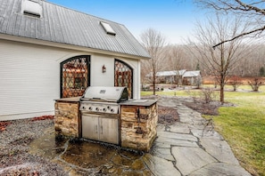 A stone barbecue grill attached to a house with a stone pathway leading to it.