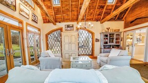 Una habitación espaciosa con vigas de madera, un candelabro, un sofá, una mesa de centro y una estantería.
