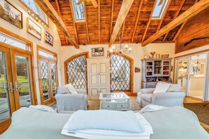 A spacious room with wooden beams, a chandelier, a sofa, a coffee table, and a bookshelf.