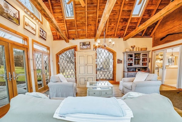 A spacious room with wooden beams, a chandelier, a sofa, a coffee table, and a bookshelf.