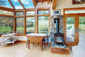 A room with a large glass window, a stone fireplace, a wooden table, and a chair.