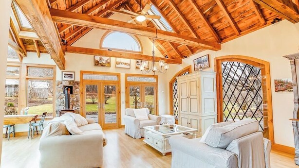 Amplia sala de estar con un alto techo de madera, ventanas grandes y una chimenea de piedra.