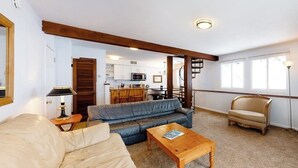 Ett vardagsrum med en soffa, ett soffbord i trä, en stol och ett kök i bakgrunden.