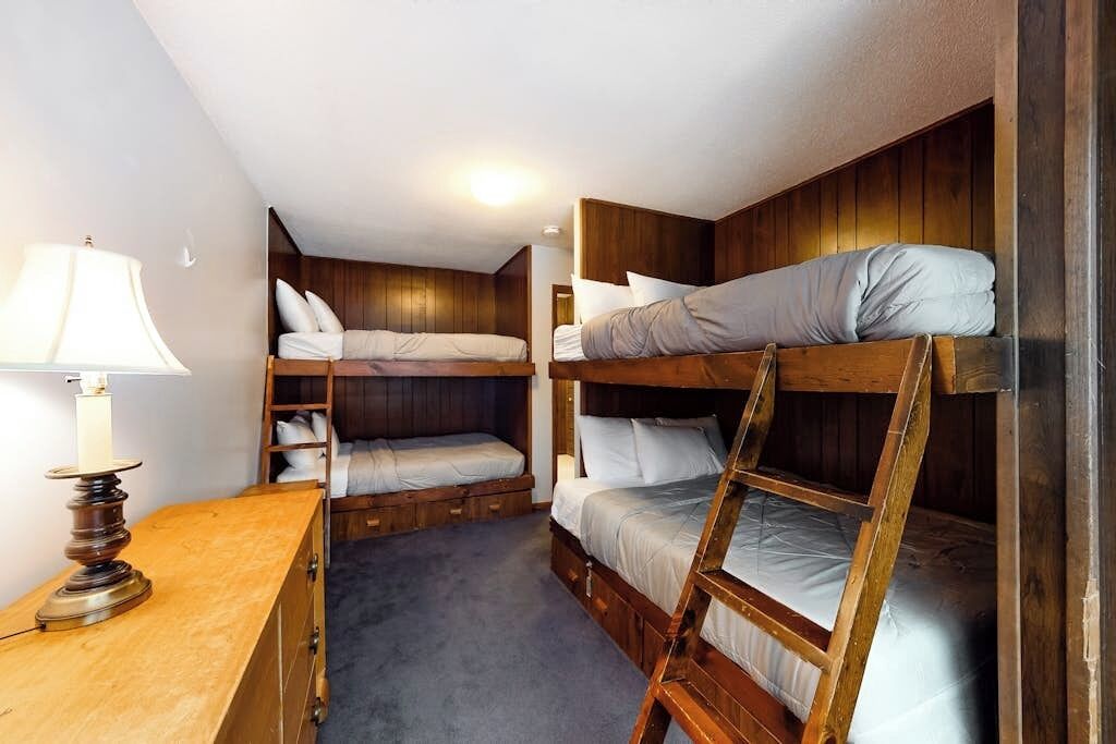Une chambre avec un lit superposé, des murs en bois, un bureau avec une lampe et un sol recouvert de moquette.