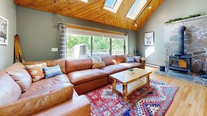 A cozy living room with a leather sectional sofa, a wooden coffee table, and a stone fireplace. - 3-story secluded home with private sauna, hot tub, pond on-site (Killington)