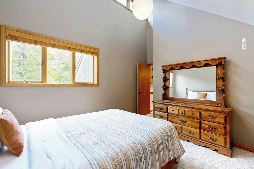 Une chambre à coucher avec un lit, une commode avec un miroir et une fenêtre.