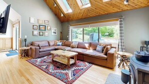 A spacious living room with a large sectional sofa, wooden flooring, and skylights. - 3-story secluded home with private sauna, hot tub, pond on-site (Killington)