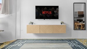 A modern living room with a mounted TV displaying the Netflix logo, a wooden cabinet below, a patterned rug, and a dining area visible in the mirror reflection. - Bellavista Galleria | Old San Juan (San Juan)