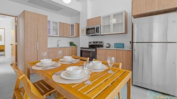 A modern kitchen with wooden cabinets, a stainless steel refrigerator, and a dining table set for four. - Bellavista Galleria | Old San Juan (San Juan)