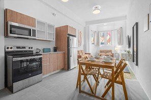A modern kitchen with stainless steel appliances, wooden cabinets, and a dining area with a table set for four. - Bellavista Galleria | Old San Juan (San Juan)