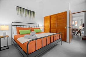A modern bedroom with a metal bed frame, orange bedding, a wooden wardrobe, and a dining area visible through an open door. - Bellavista Galleria | Old San Juan (San Juan)