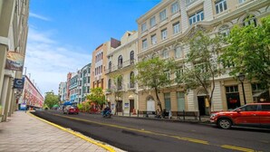 A street lined with multi-story buildings, a sidewalk, and a few parked cars. - Bellavista Galleria | Old San Juan (San Juan)