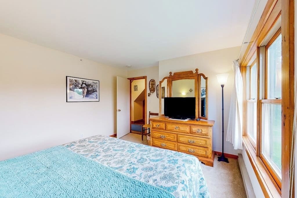A bedroom with a bed, dresser, mirror, and a window.
