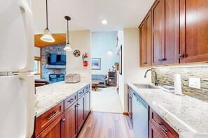 A kitchen with wooden cabinets, granite countertops, pendant lighting, and a stone backsplash. - Trail Creek 31 | Walk-to-lift condo in Killington with pool, hot tub, gym, sauna (Killington)