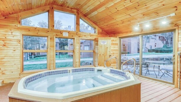 Eine Holzhütte mit Whirlpool, großen Fenstern und einer Terrassenfläche.