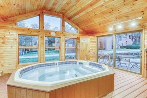 Eine Holzhütte mit Whirlpool, großen Fenstern und einer Terrassenfläche.