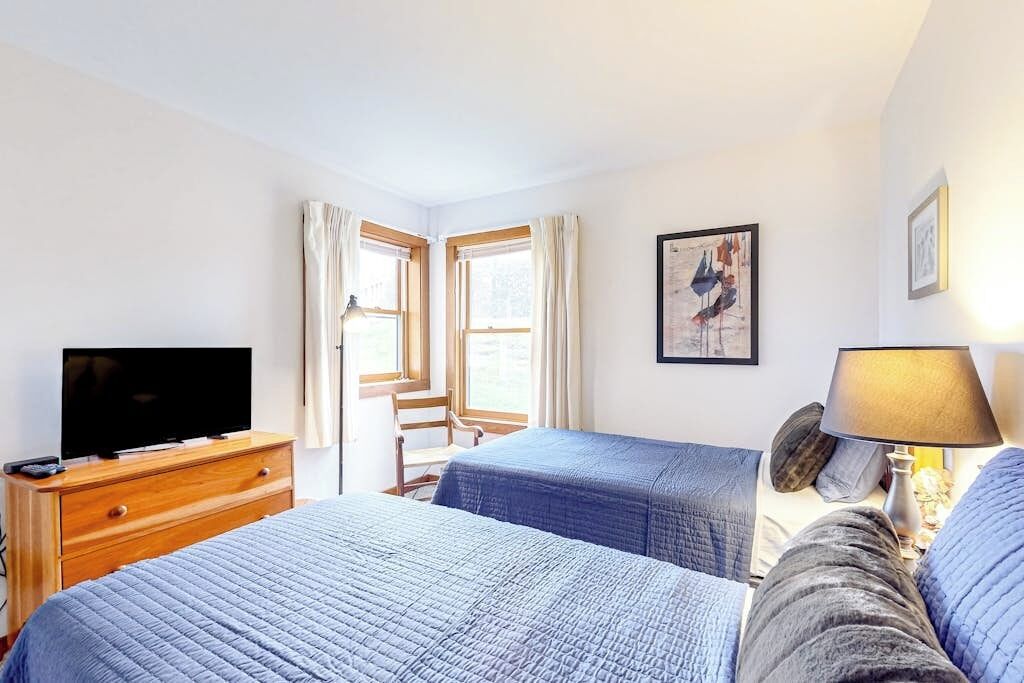 A hotel room with a bed, a TV on a wooden dresser, a chair, and a window with curtains.