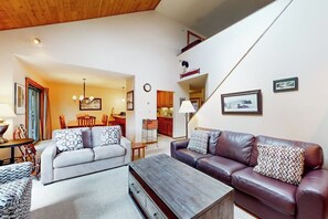 A living room with a sofa, a coffee table, and a dining area with chairs and a table. - Two-story, walk-to-lift condo with indoor pool, hot tub, sauna, gym & game room (Killington)