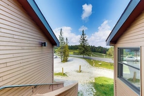 A view from a window of a building with a wooden exterior, a gravel driveway, and a road in the background. - Two-story, walk-to-lift condo with indoor pool, hot tub, sauna, gym & game room (Killington)