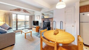 Una sala de estar con sofá, mesa de centro, mesa de comedor con sillas, chimenea y televisor.