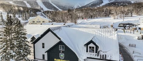 Een lodge met een met sneeuw bedekte dak, een skilift en een bergachtige achtergrond.