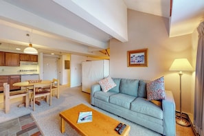 A living room with a sofa, a coffee table, a dining table with chairs, a lamp, and a picture on the wall. - 5th-floor mountain-view condo, easy access to the slopes free shuttle or walk (Killington)